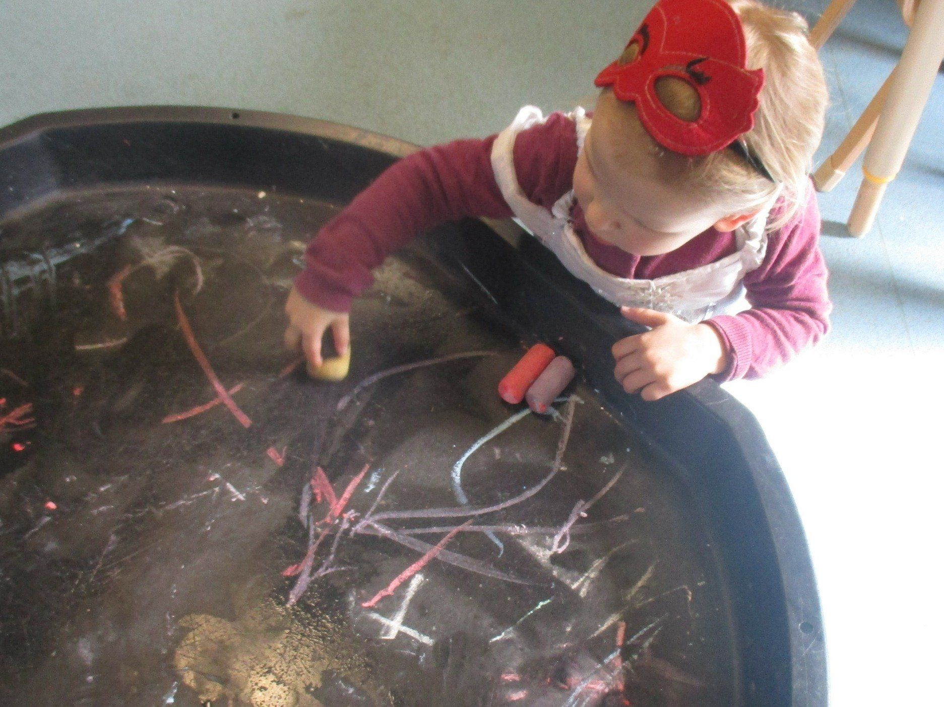A little girl wearing a red flower headband is playing in a bucket of water