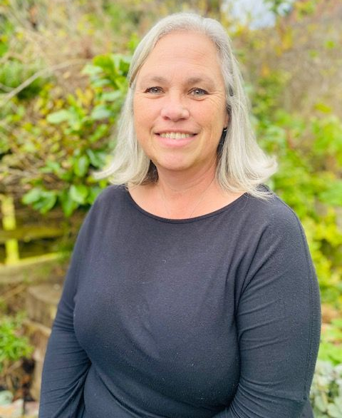 A woman in a black shirt is sitting next to a tree.