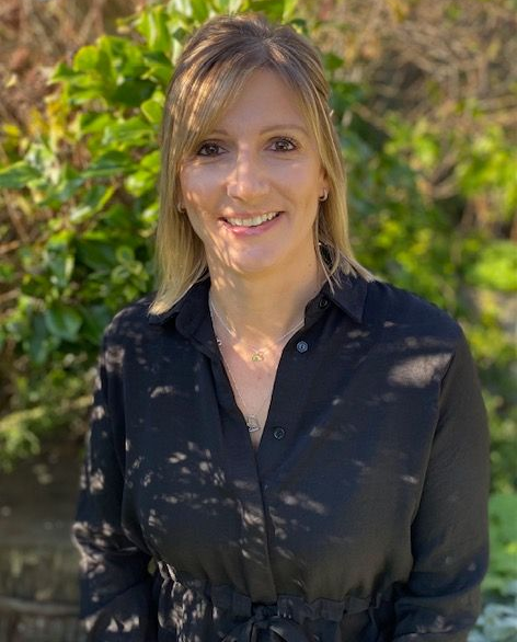 A woman in a black dress is smiling and standing in front of a blue wall.