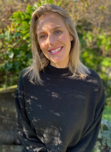 A woman wearing glasses and a black shirt is smiling in front of a tree.