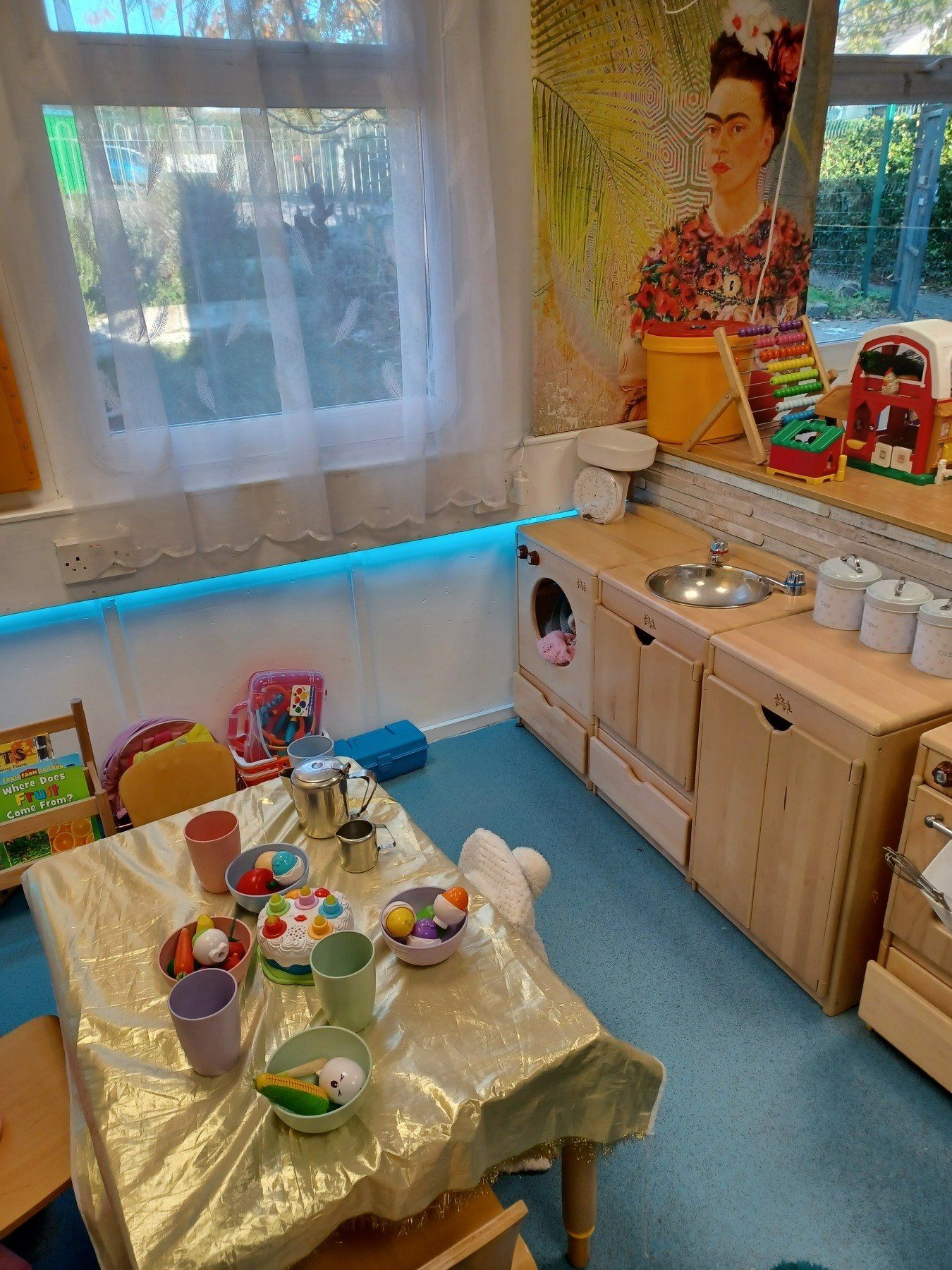 A room with a table and chairs and a painting of frida kahlo on the wall.