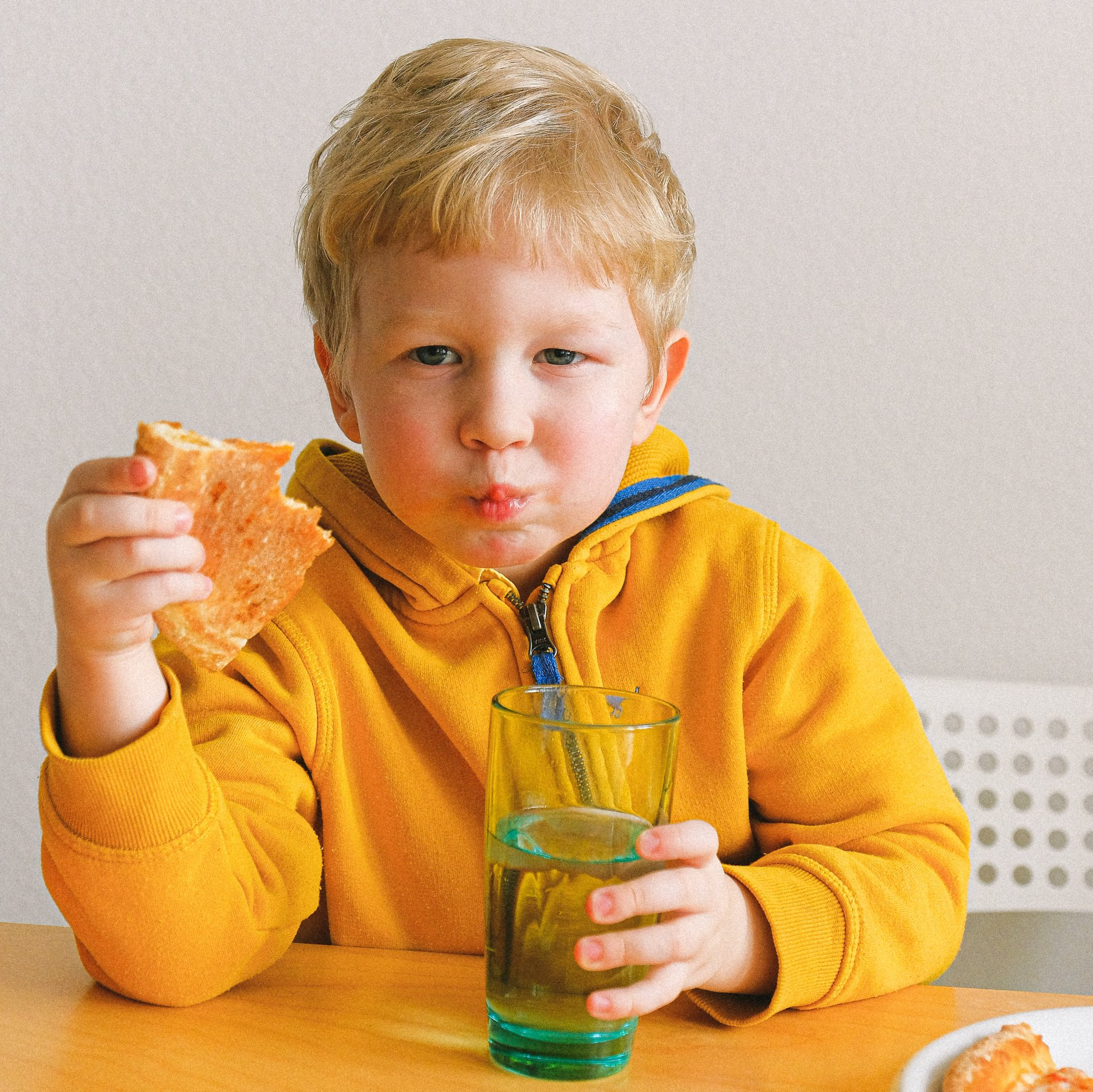 Little boy eating lunch and holding a glass of water