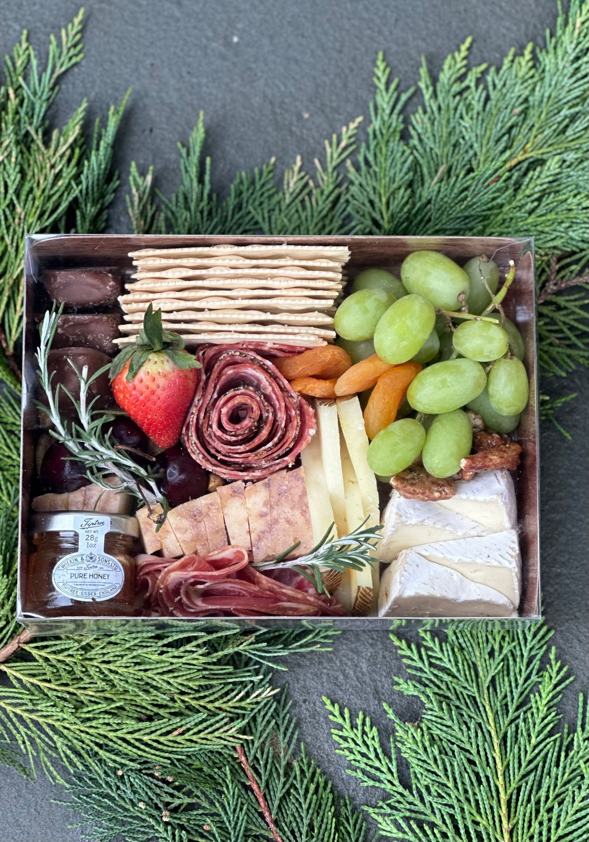 a box filled with a variety of food including crackers grapes and a strawberry