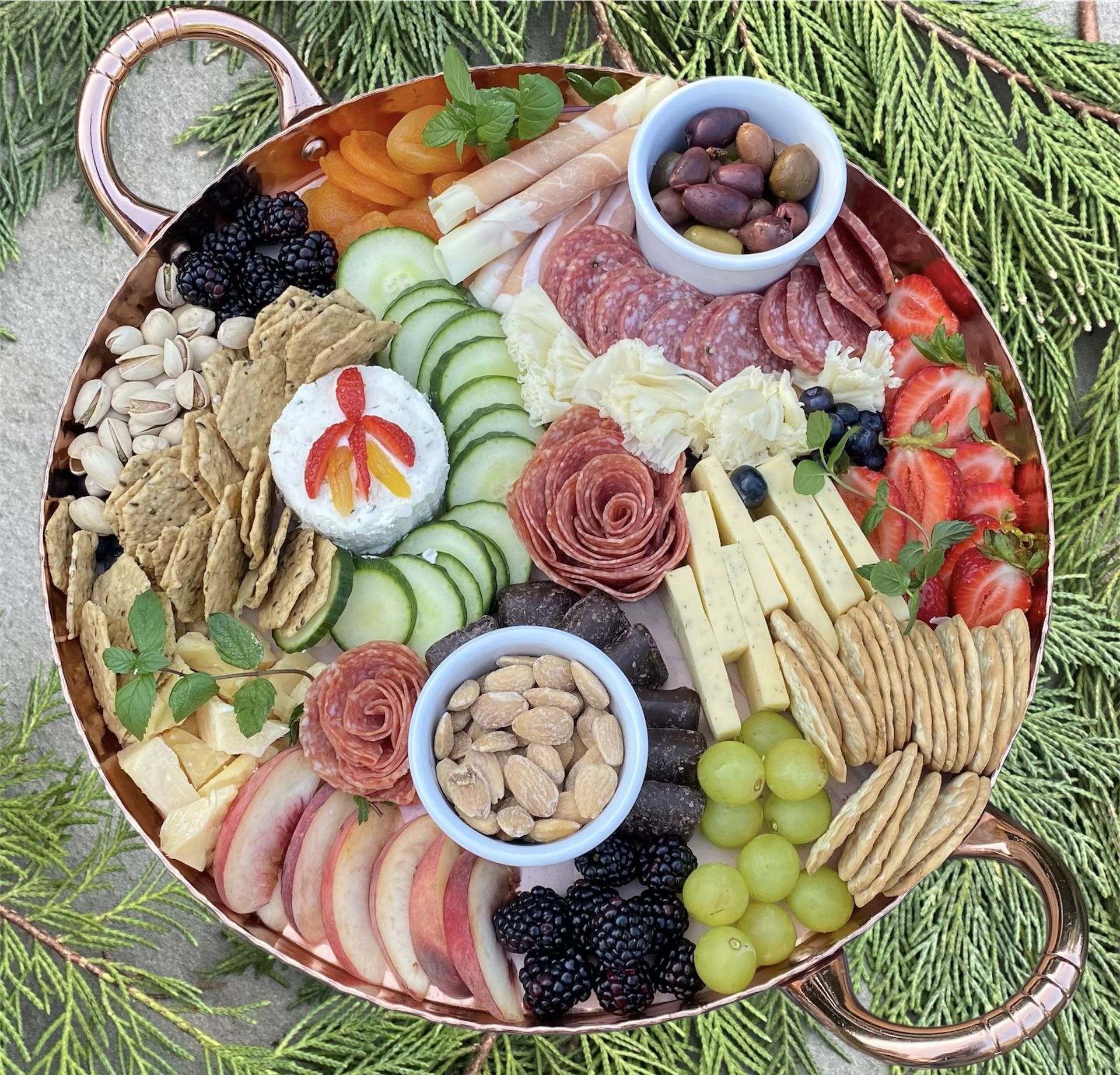 a copper bowl filled with a variety of snacks including crackers cheese and fruit