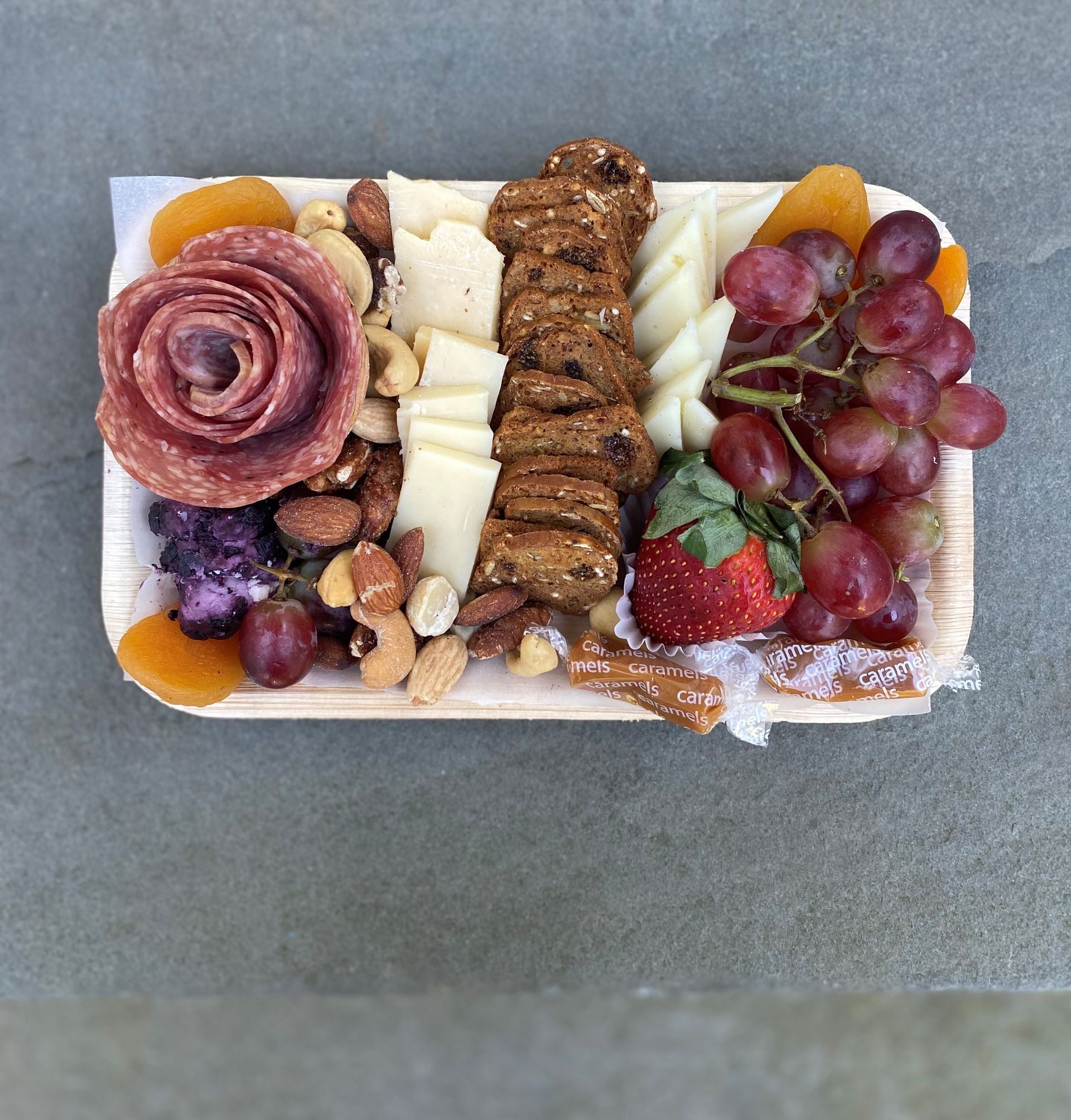 a wooden tray filled with cheese grapes nuts and crackers charcuterie board
