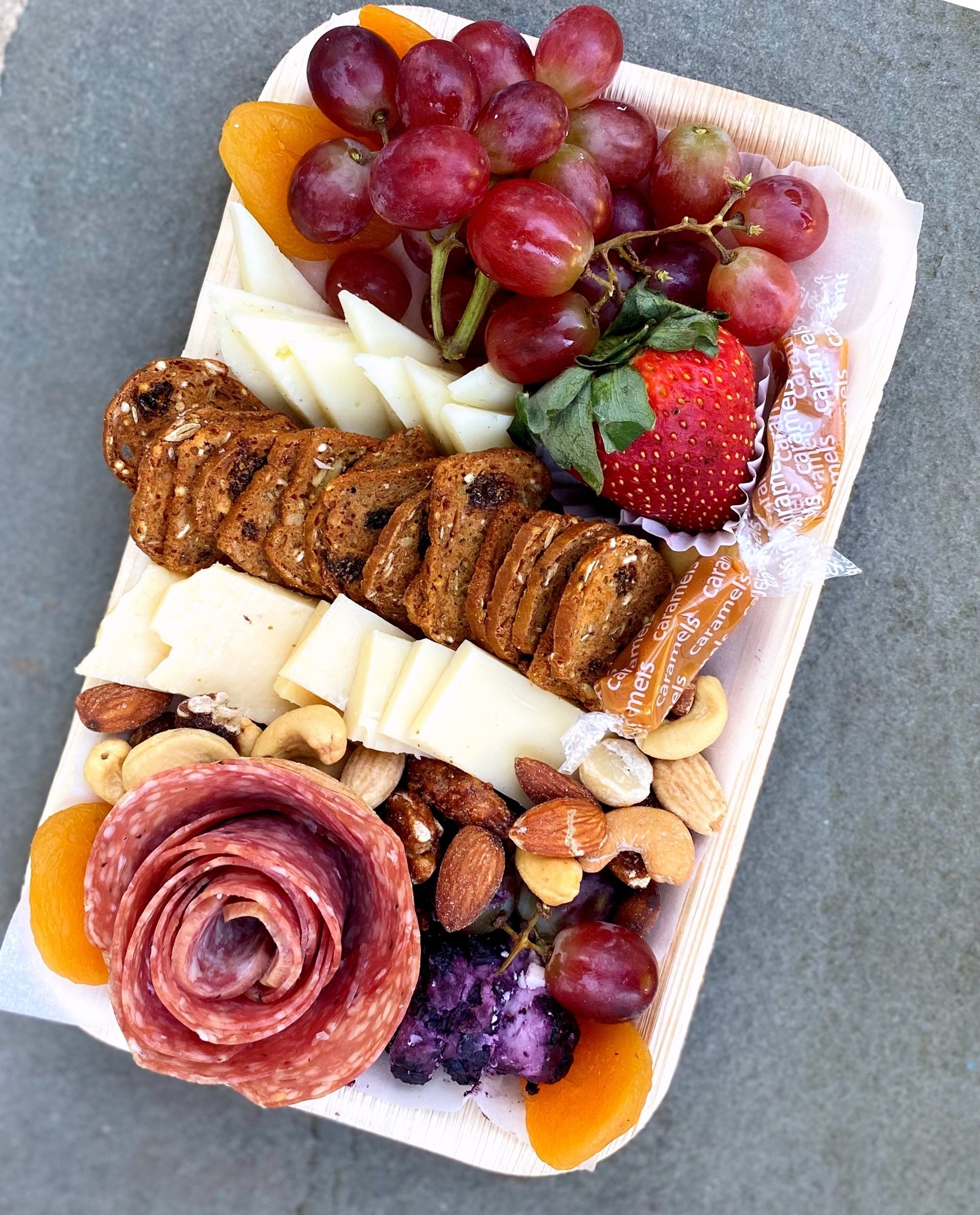 a tray of food including grapes nuts and salami