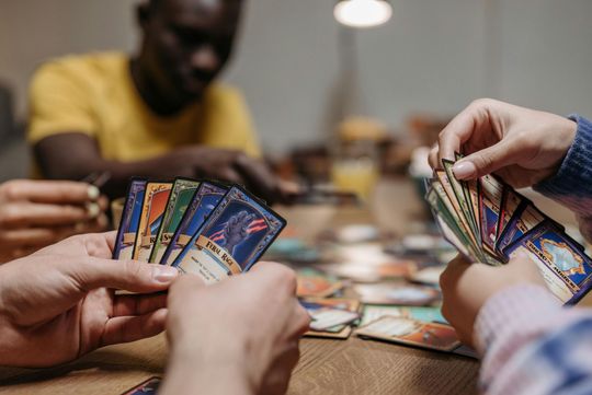 Hands holding colorful trading cards over a table during a card game round