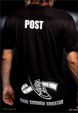 Person wearing a black t-shirt with "POST" printed on the upper back and a film reel logo.