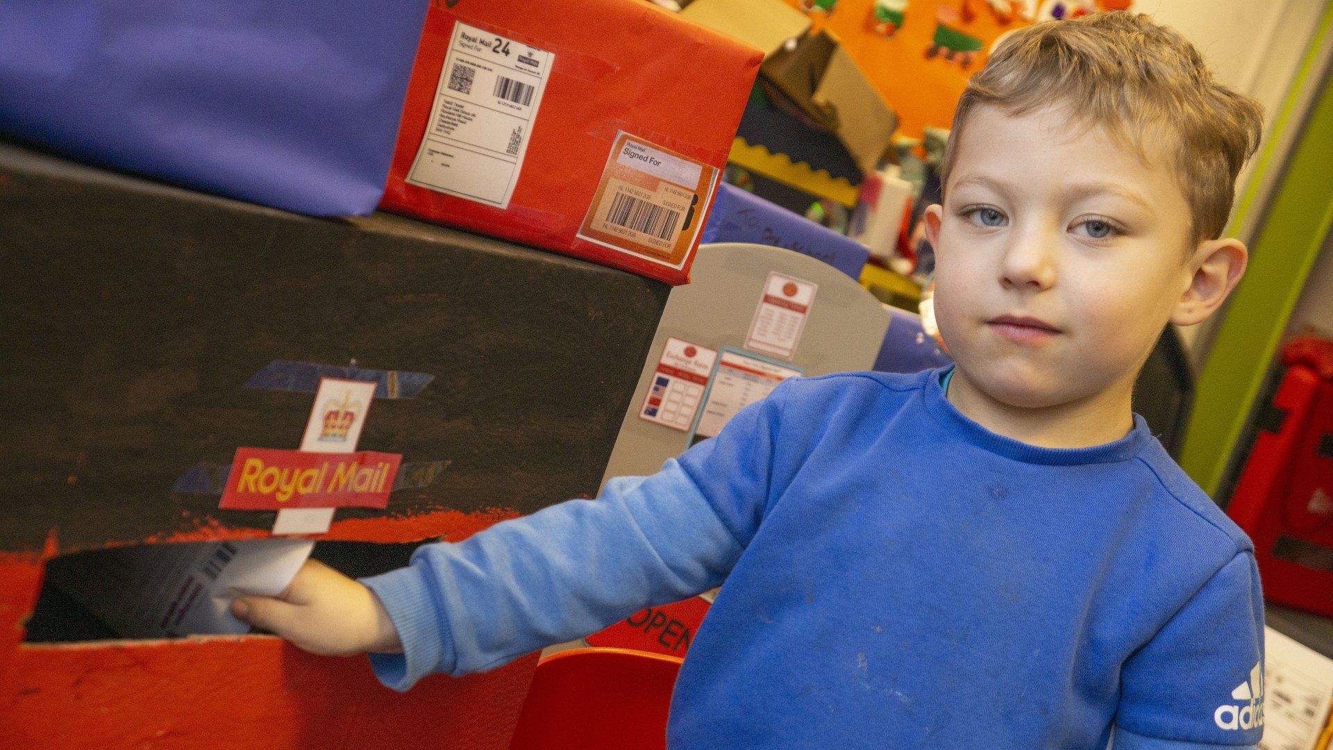 Boy in blue shirt dropping mail into a Royal Mail postbox replica.