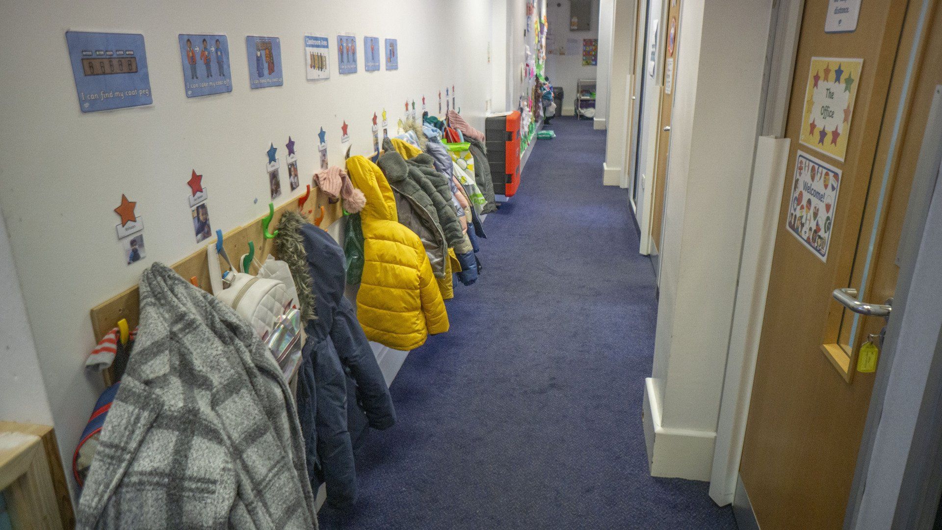 Hallway with blue carpet, coat rack, and closed wooden doors.