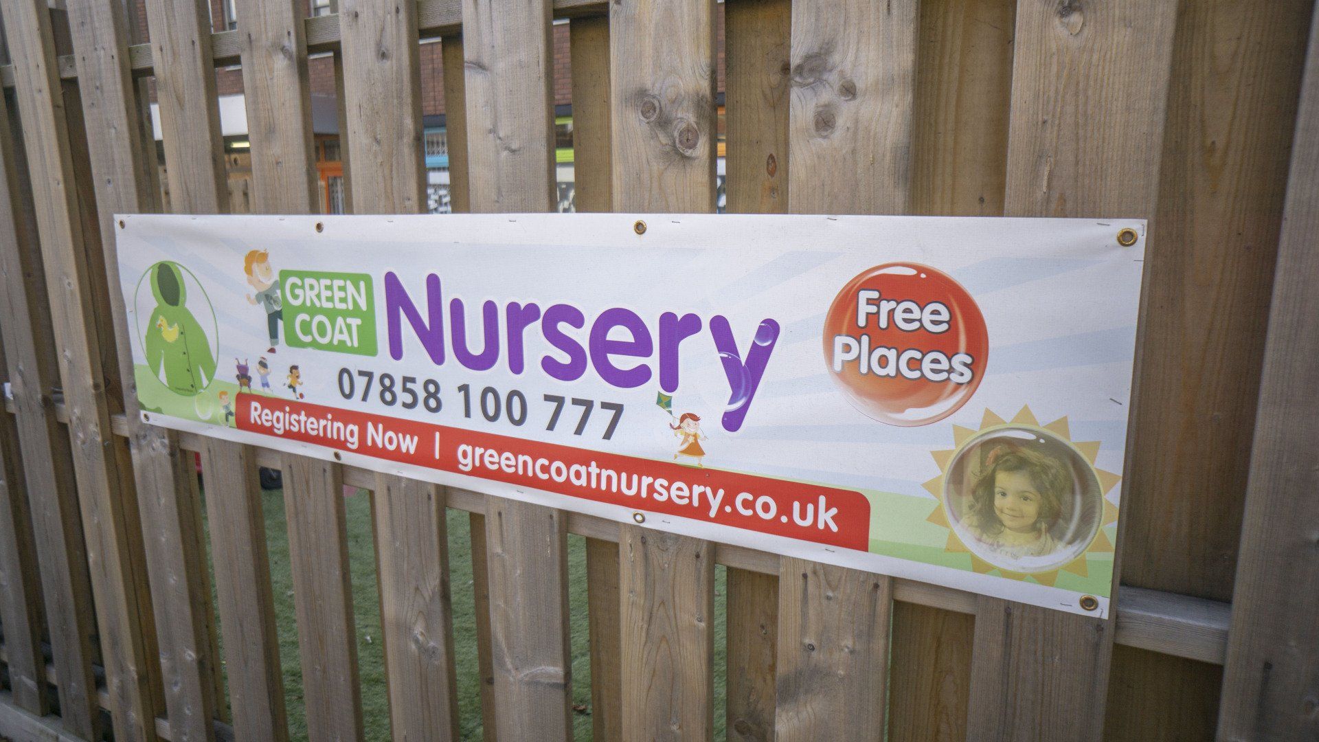 Banner for Green Coat Nursery on a wooden fence, advertising 