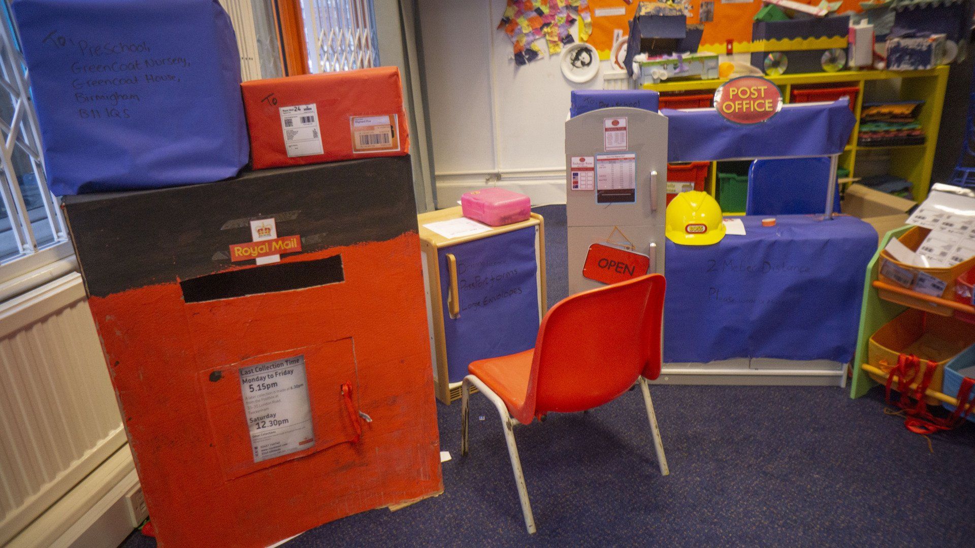 A child's play area designed as a post office with mailboxes, a counter, and a red chair.