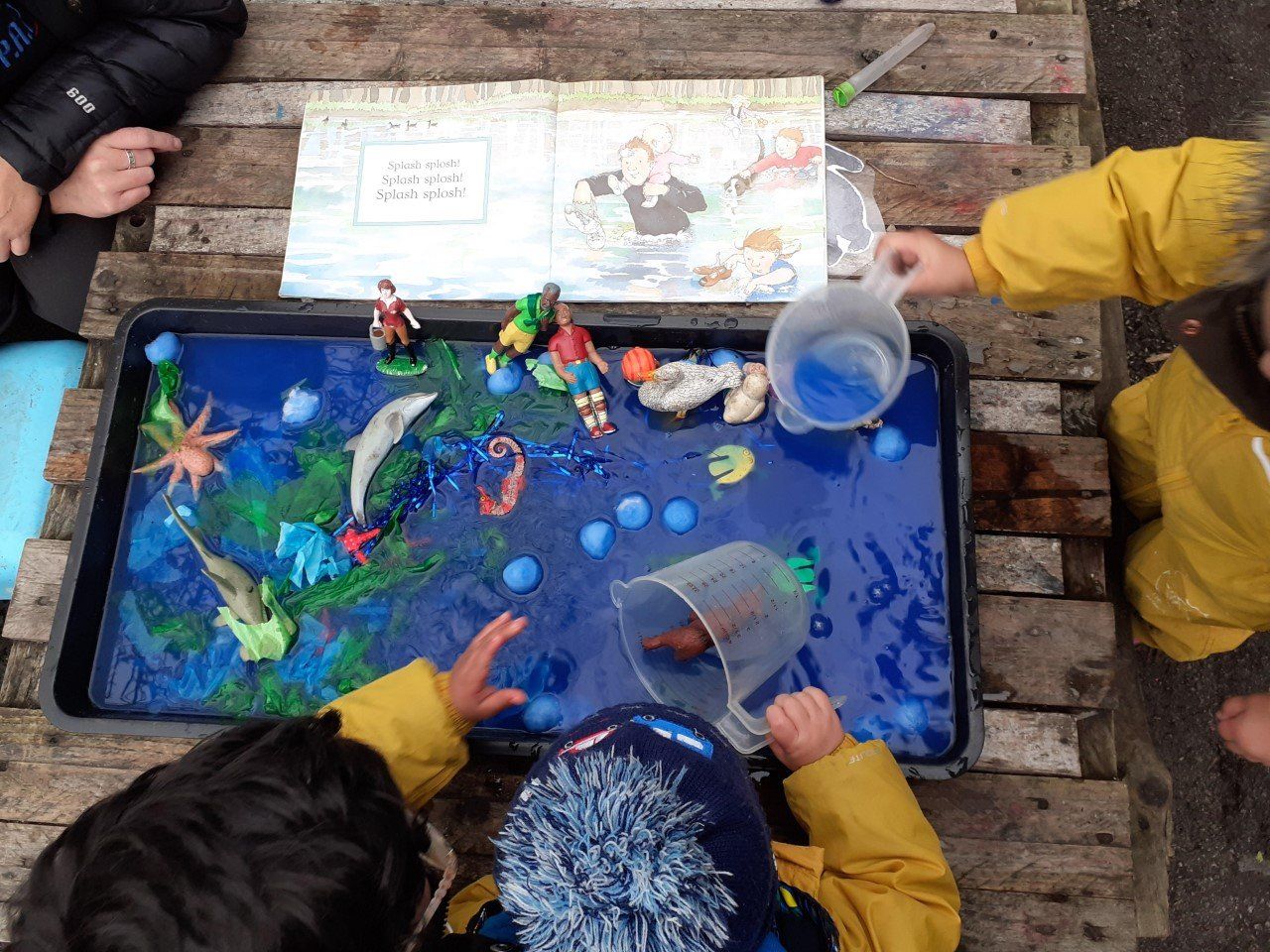 Children playing with toy sea creatures and blue water in a tray, pouring water.