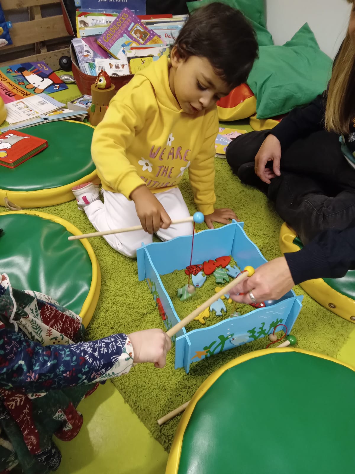 Child playing fishing game with help from adults.