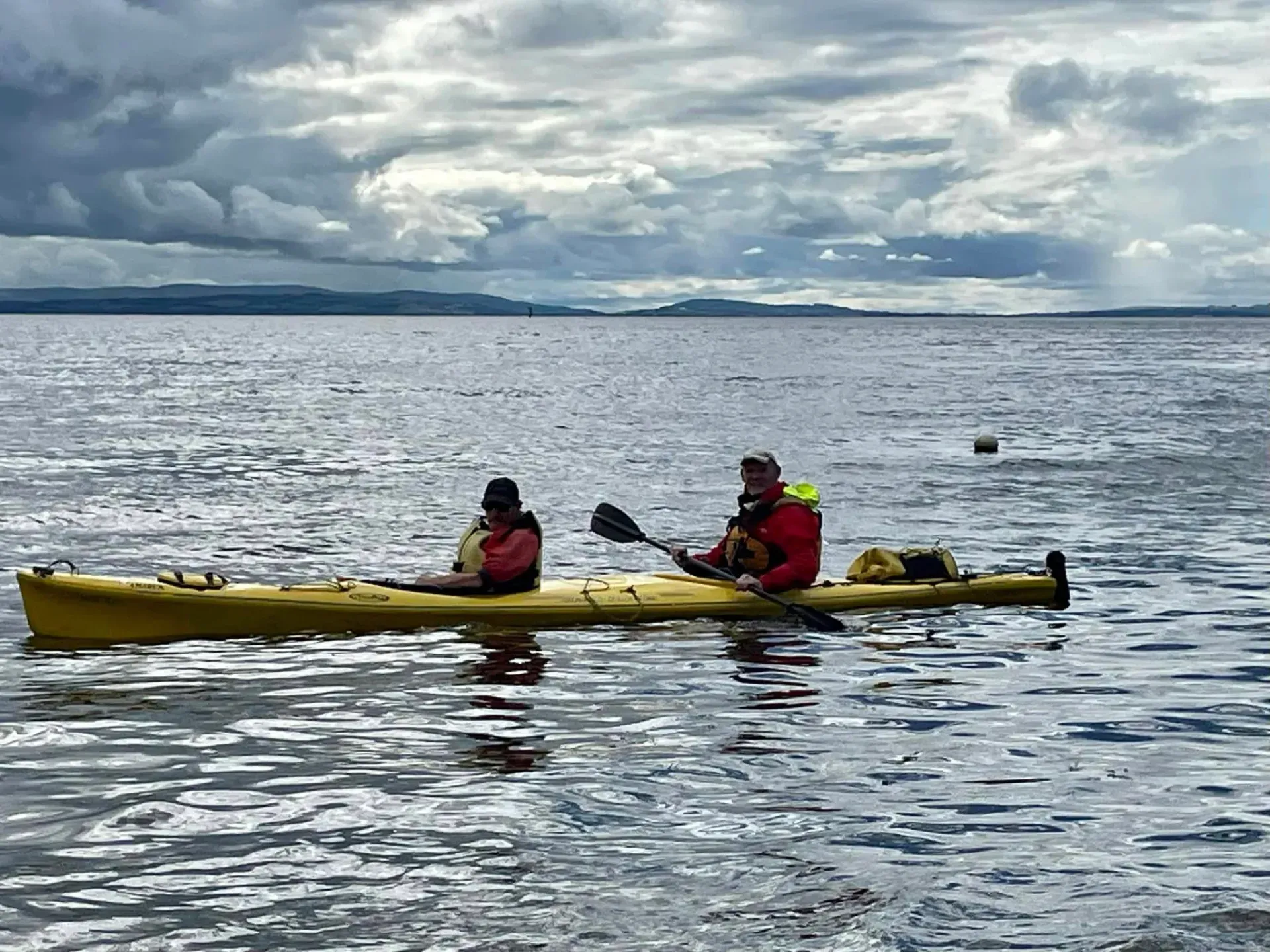 Two people are in a yellow kayak on a cloudy day