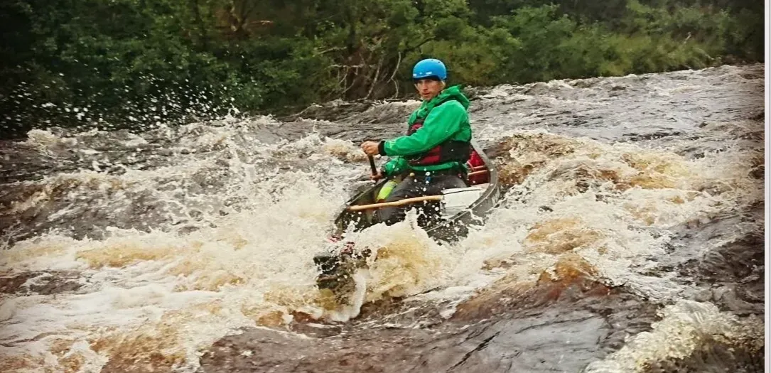 A man is riding a kayak through a flooded river.