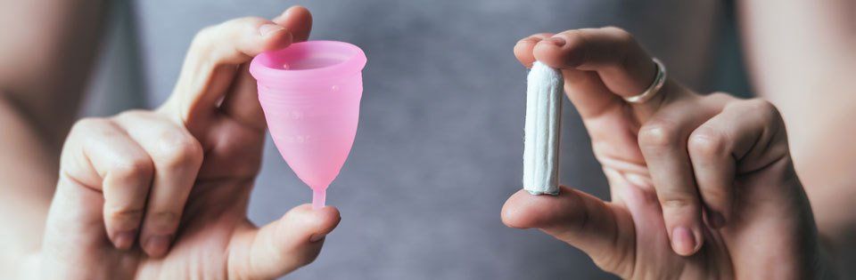 Woman hands holding pink menstrual cup and OB - female hygiene products 