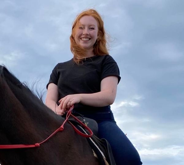 A woman in a black shirt is riding a brown horse
