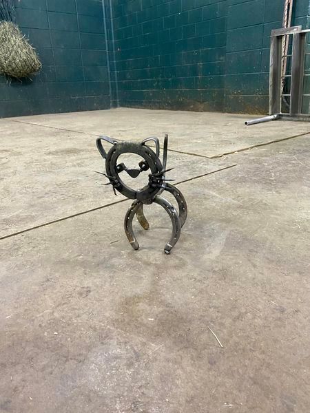 A cat made out of horseshoes is sitting on a concrete floor.