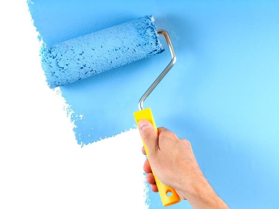 A person is painting a wall with a blue paint roller.