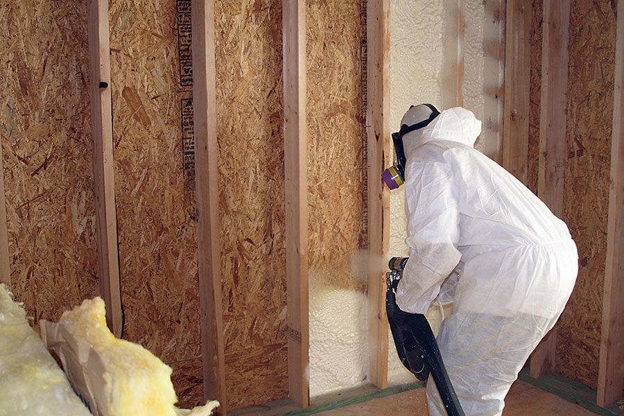 A man in a protective suit is spraying insulation on a wall.