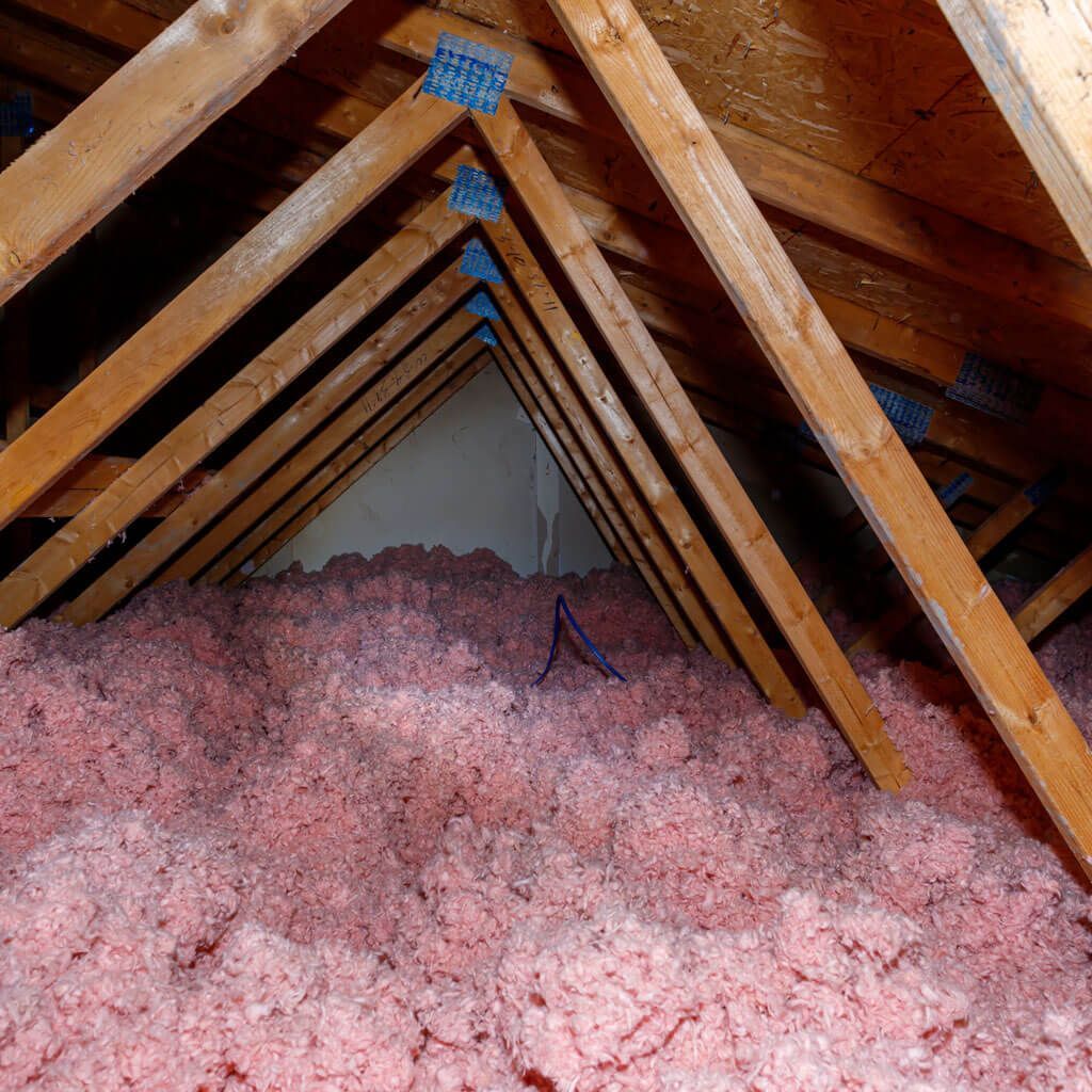 An attic filled with pink insulation and wooden beams.