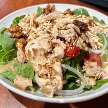 a salad with chicken , spinach , tomatoes , onions and walnuts on a plate on a table