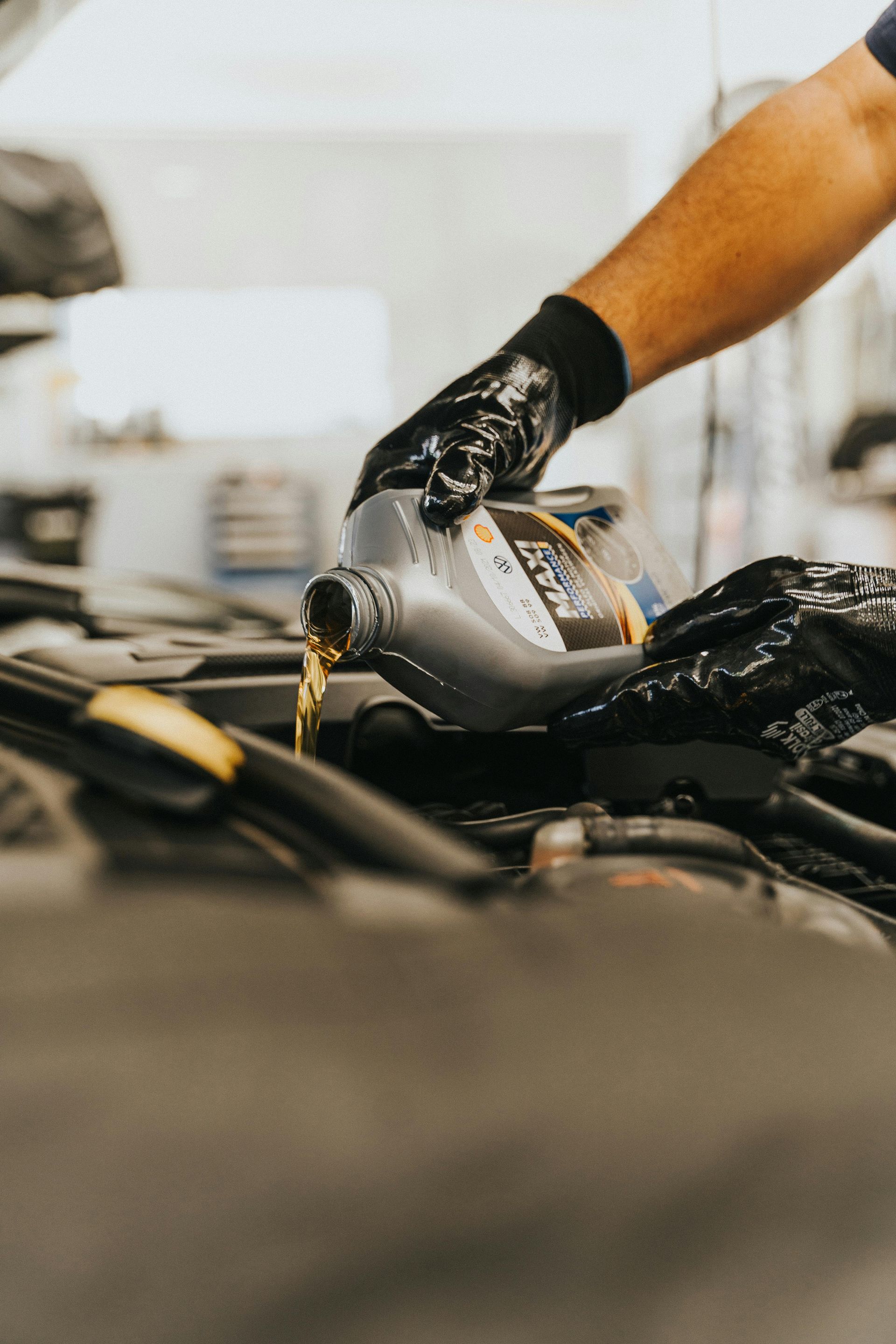 Gloved hands pouring motor oil from a gray bottle into a car engine bay