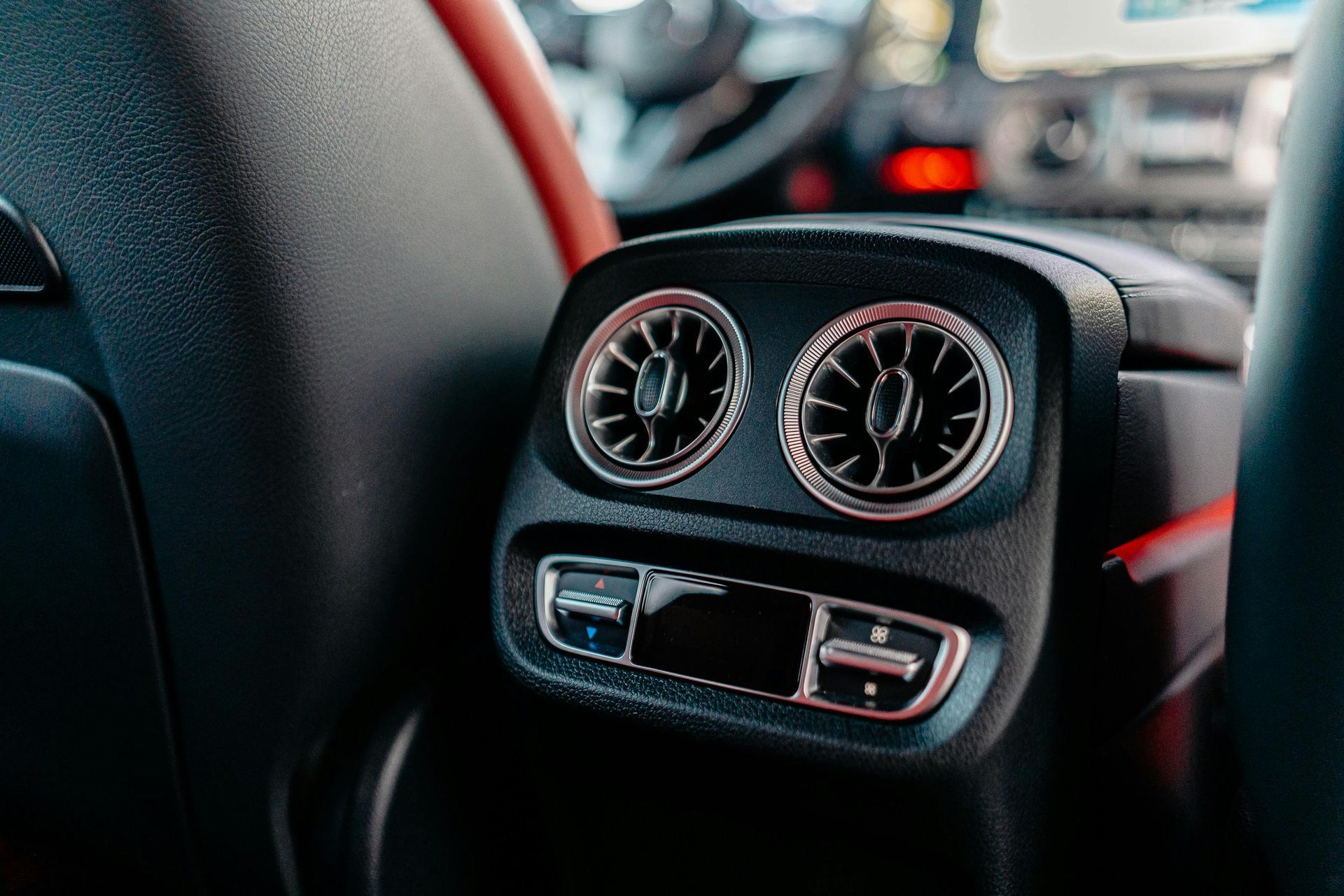Car rear-seat air vents and climate controls on a black dashboard with red accent lighting