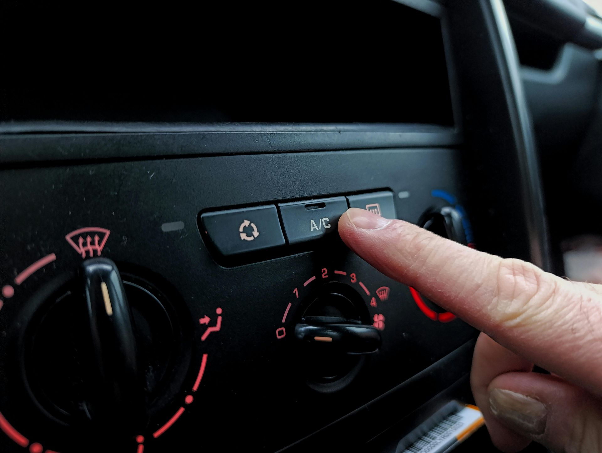 Hand pressing a car dashboard climate control button with red-lit controls and fan dial
