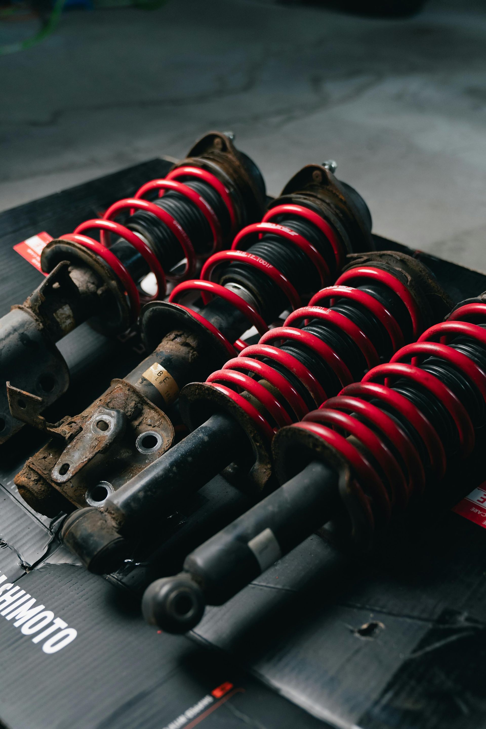 Red coilover suspension shocks with black mounts on a dark surface.
