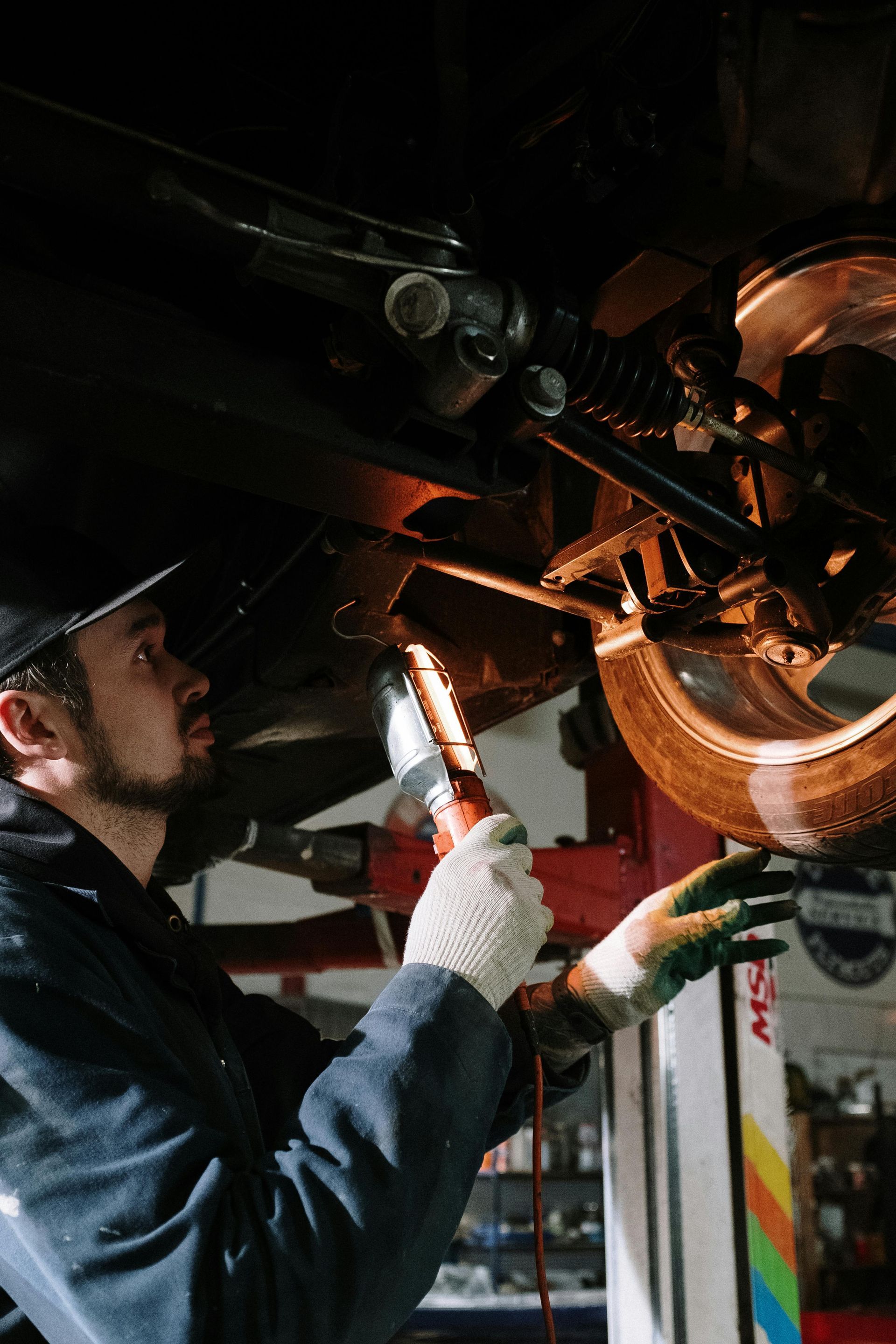 Mechanic inspecting motorcycle undercarriage with a flashlight in a dim garage
