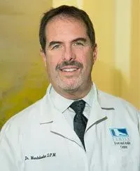 A smiling doctor in a lab coat with a stethoscope around his neck.