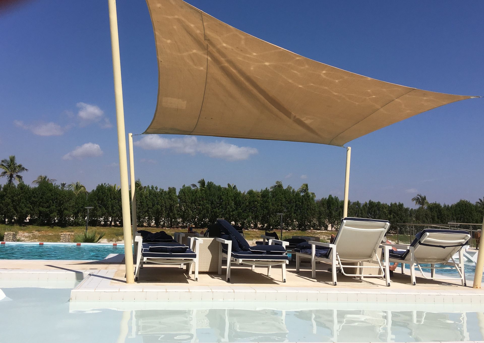 A swimming pool with chairs under a shade sail | Cordova & Pasadena, MD | Shoreline Awning & Trim