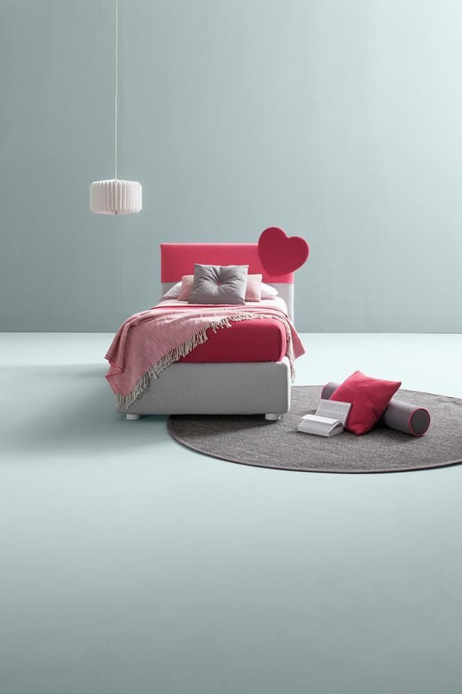 Camera da letto minimalista con letto rosa, testiera a forma di cuore e tappeto rotondo su un pavimento chiaro.