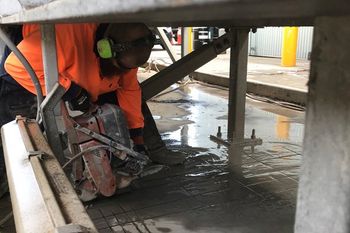 man cutting concrete under steel truss