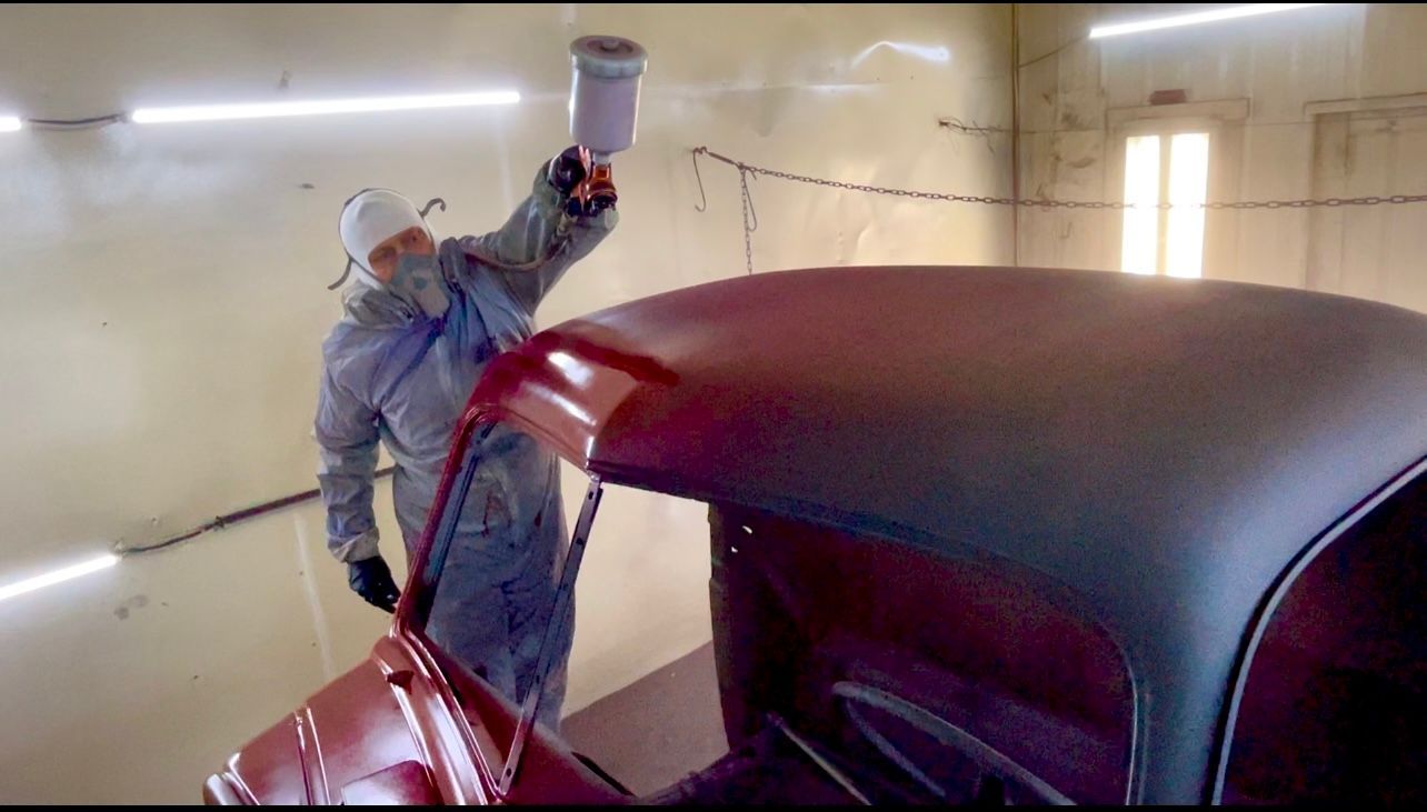 A man is spray painting the roof of a red car