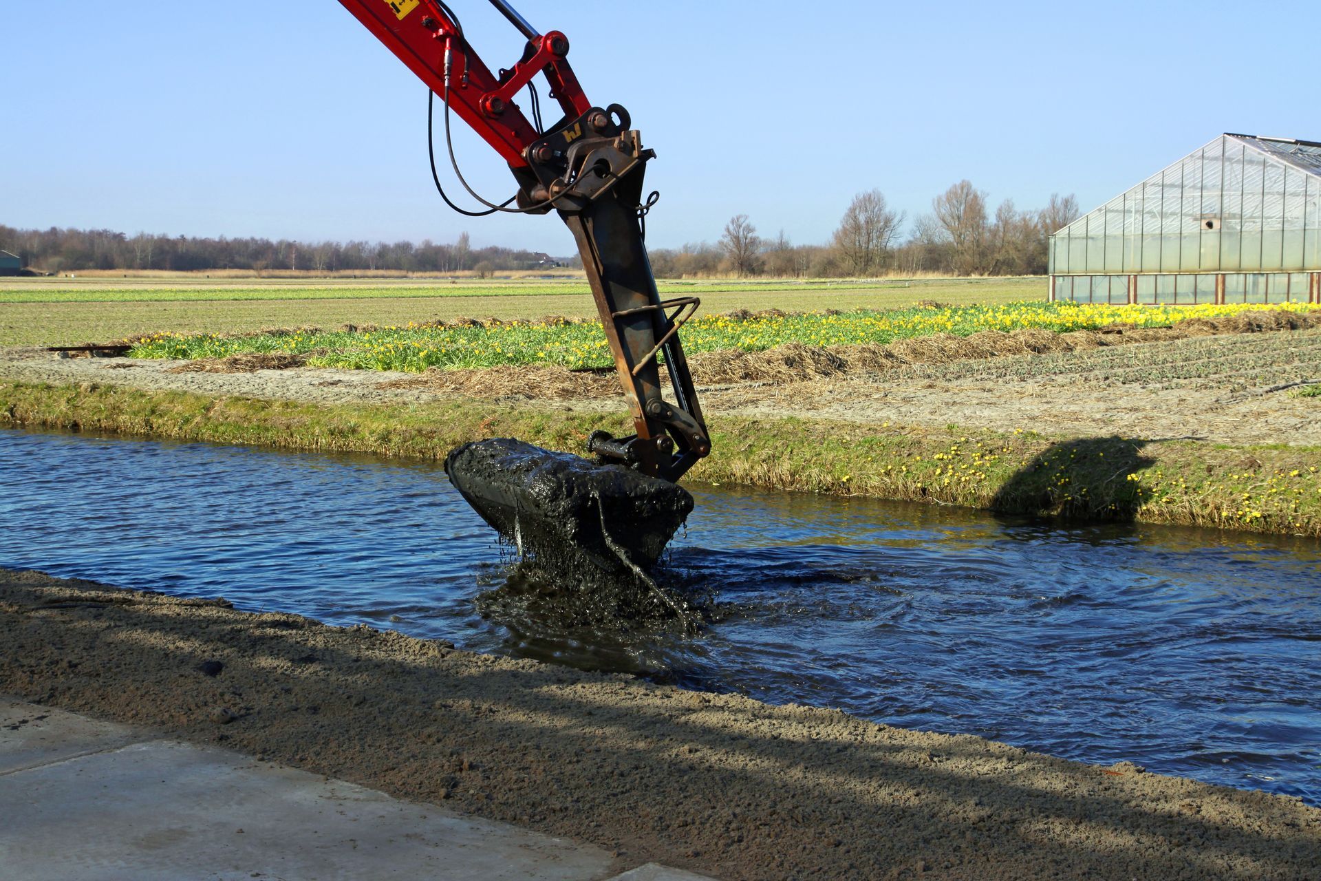 Dredging of a canal in the flower bulb growing region in early spring with a backhoe crane depositing the dredging spoil in a tipper trailer