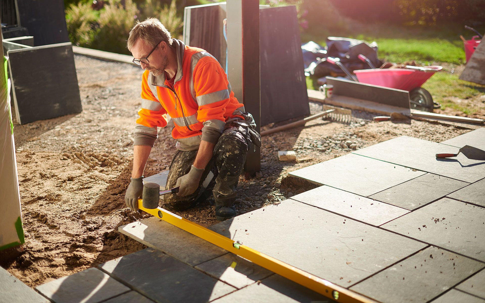 A man is kneeling down while using a level on a patio.