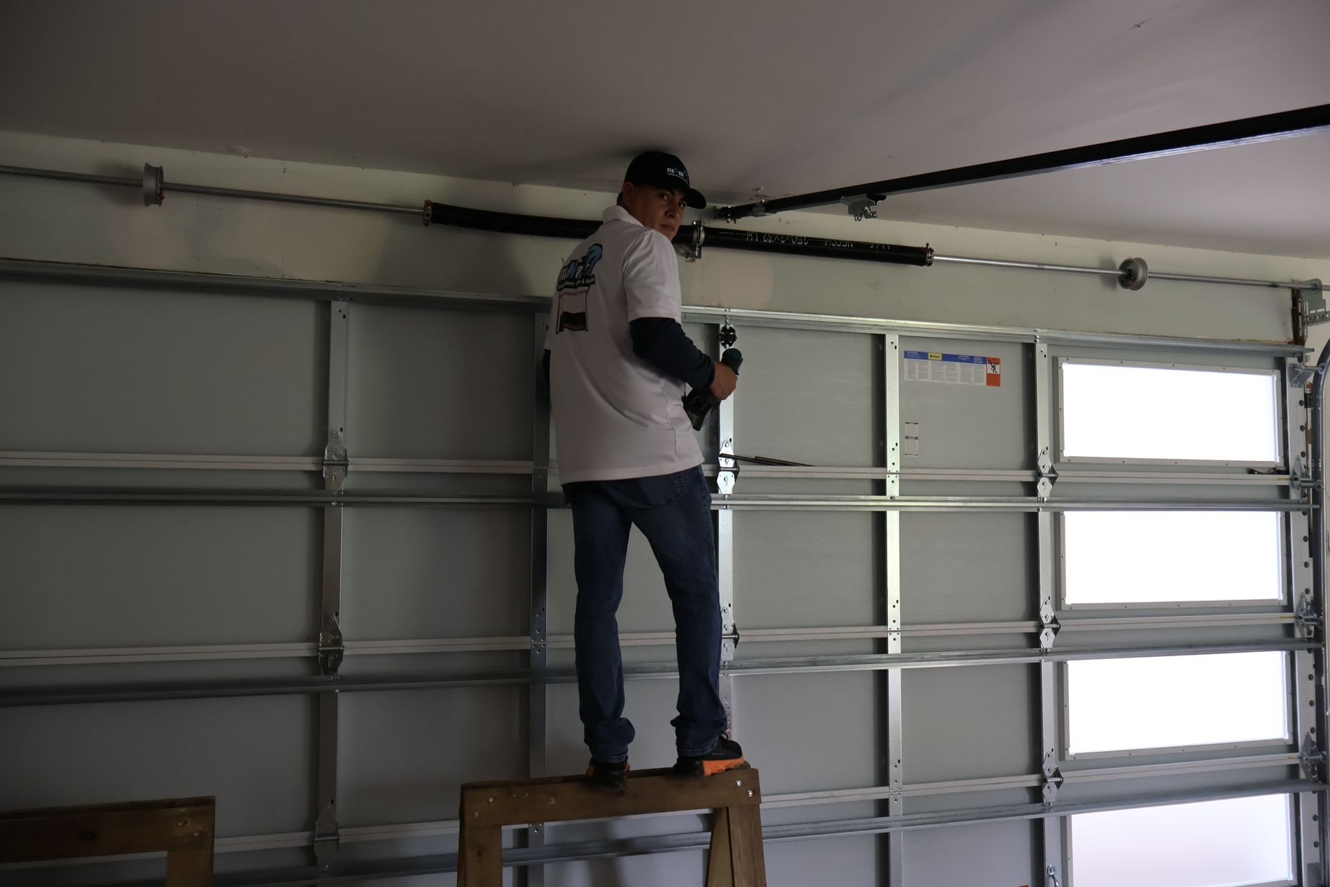 Person standing on a stool working on a garage door opener inside a garage