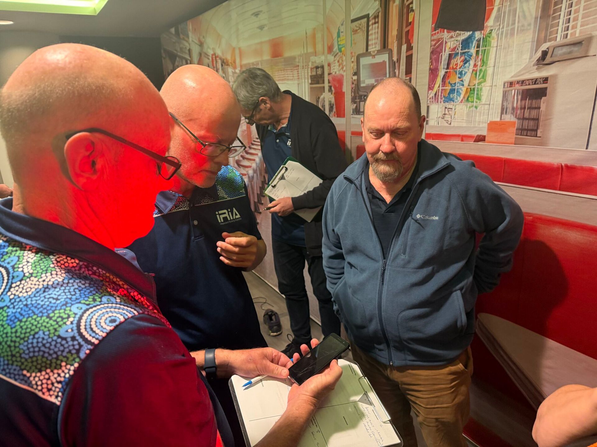 Four men examining an object indoors, as if in a crime scene.
