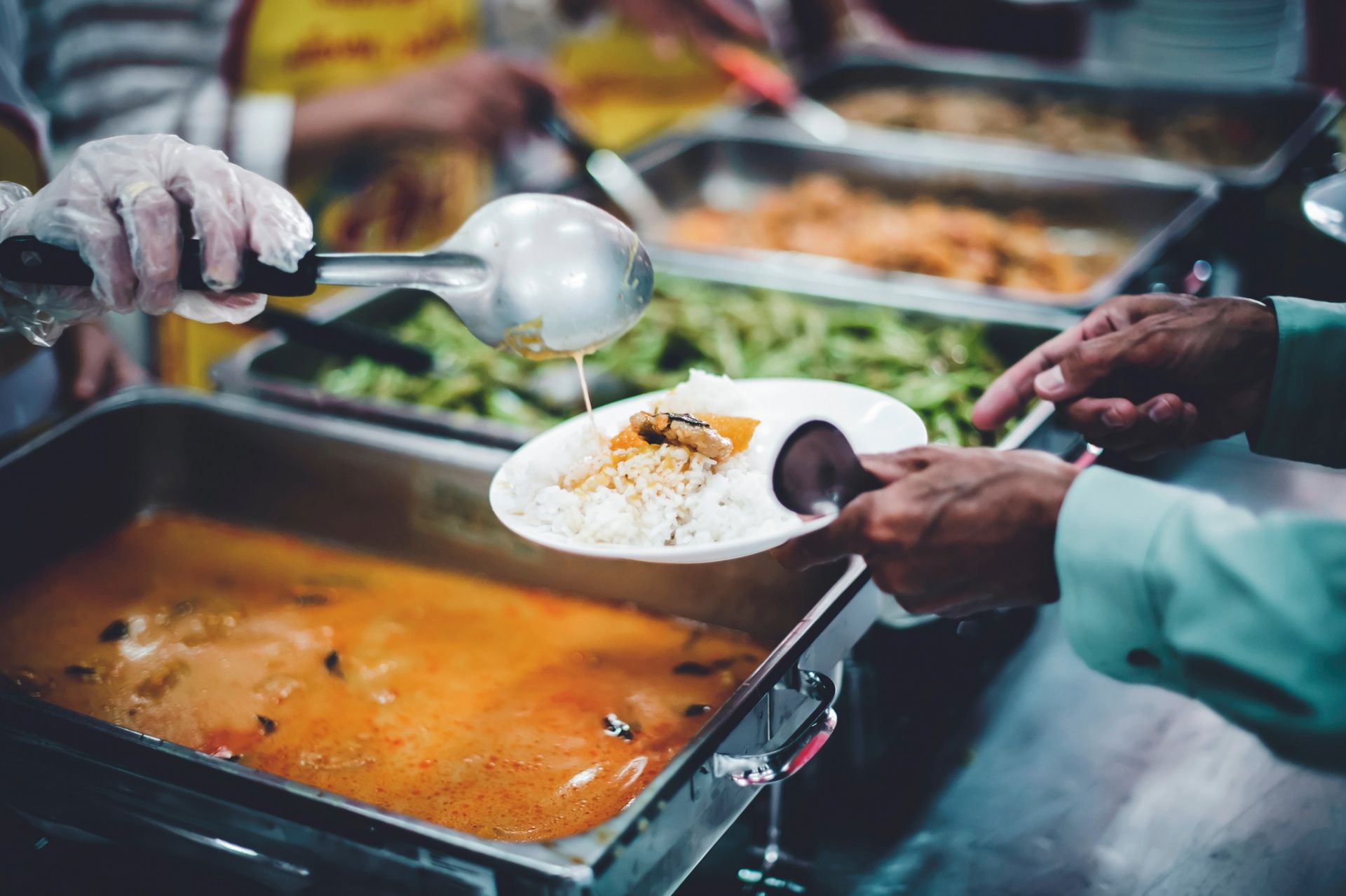 Person serving food from a buffet line onto a plate.