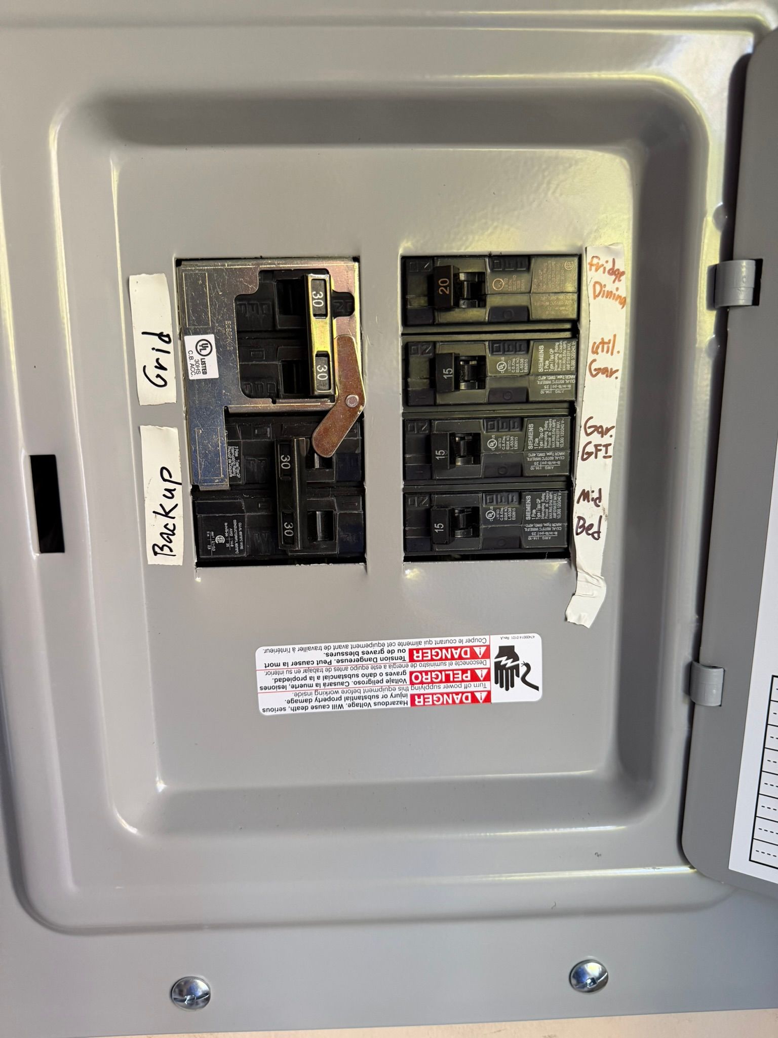 Electrical breaker box with labeled switches, inside a gray metal cabinet.