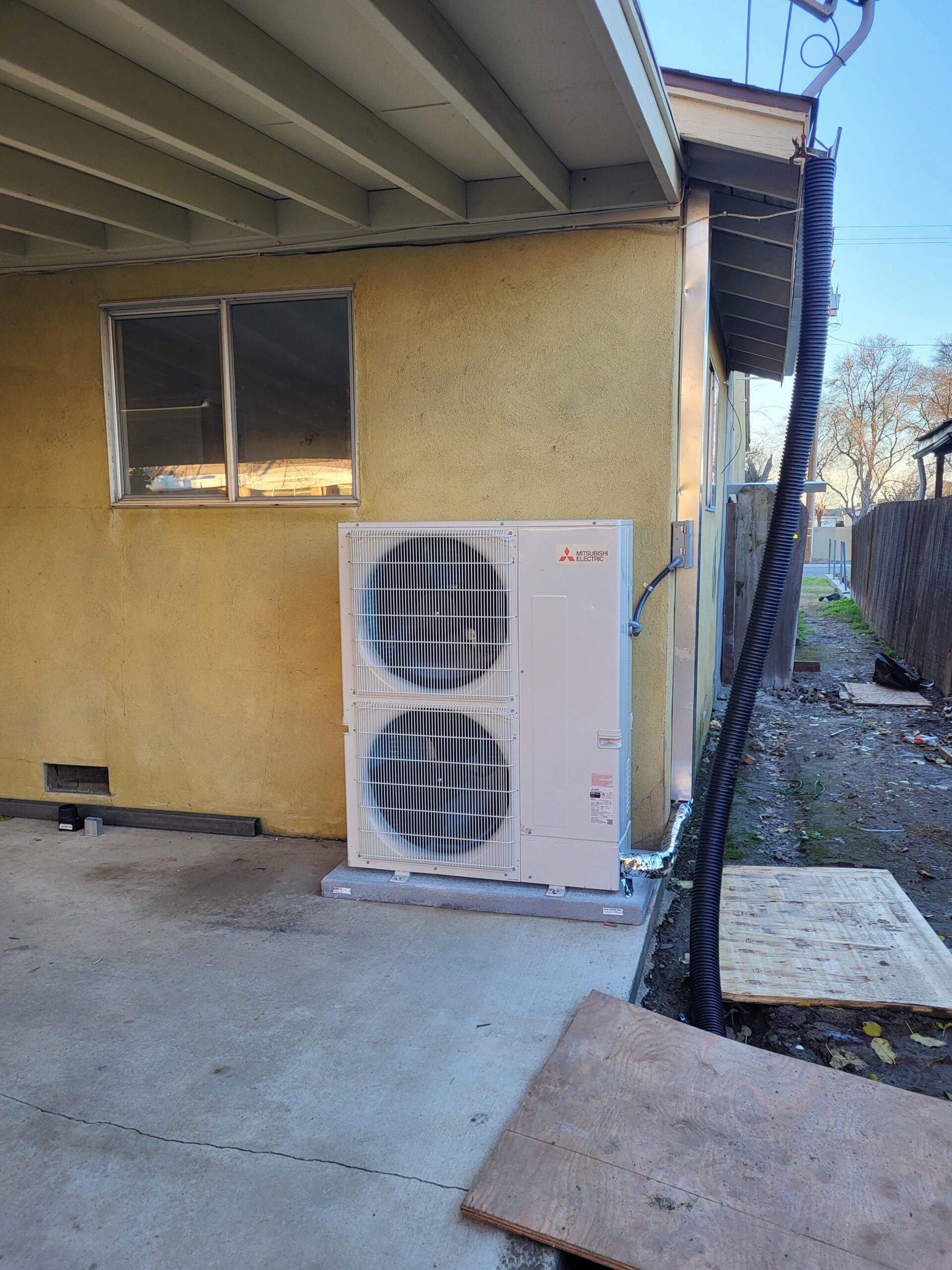 A mitsubishi air conditioner is sitting outside of a house.