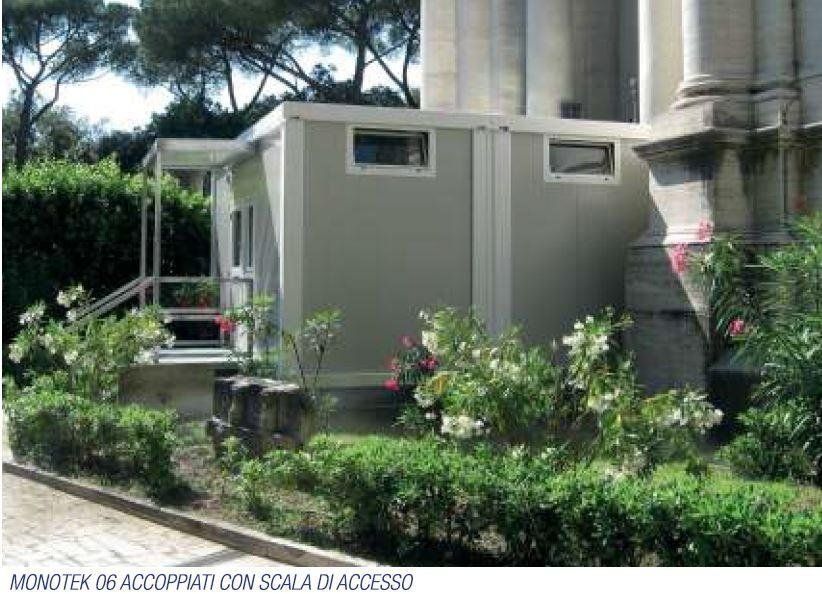 Un piccolo edificio con portico è circondato da cespugli e alberi.