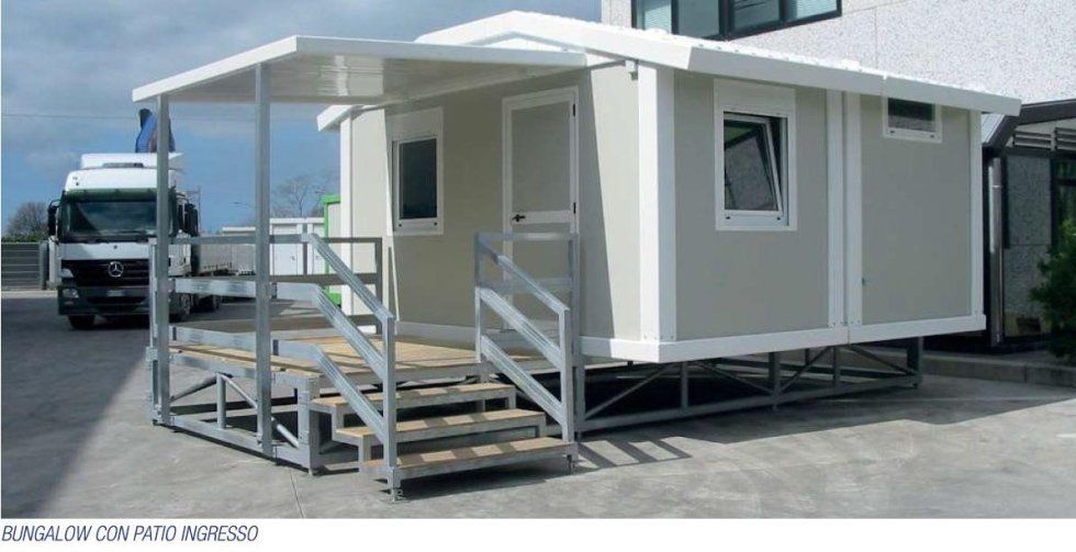 Davanti ad un edificio è parcheggiata una casetta con scale e tettoia.