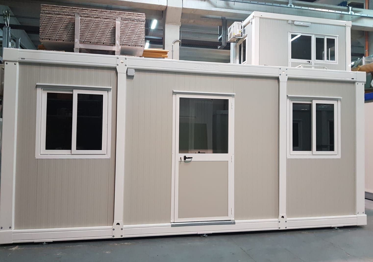 Una casa container con due finestre e una porta si trova in un magazzino.