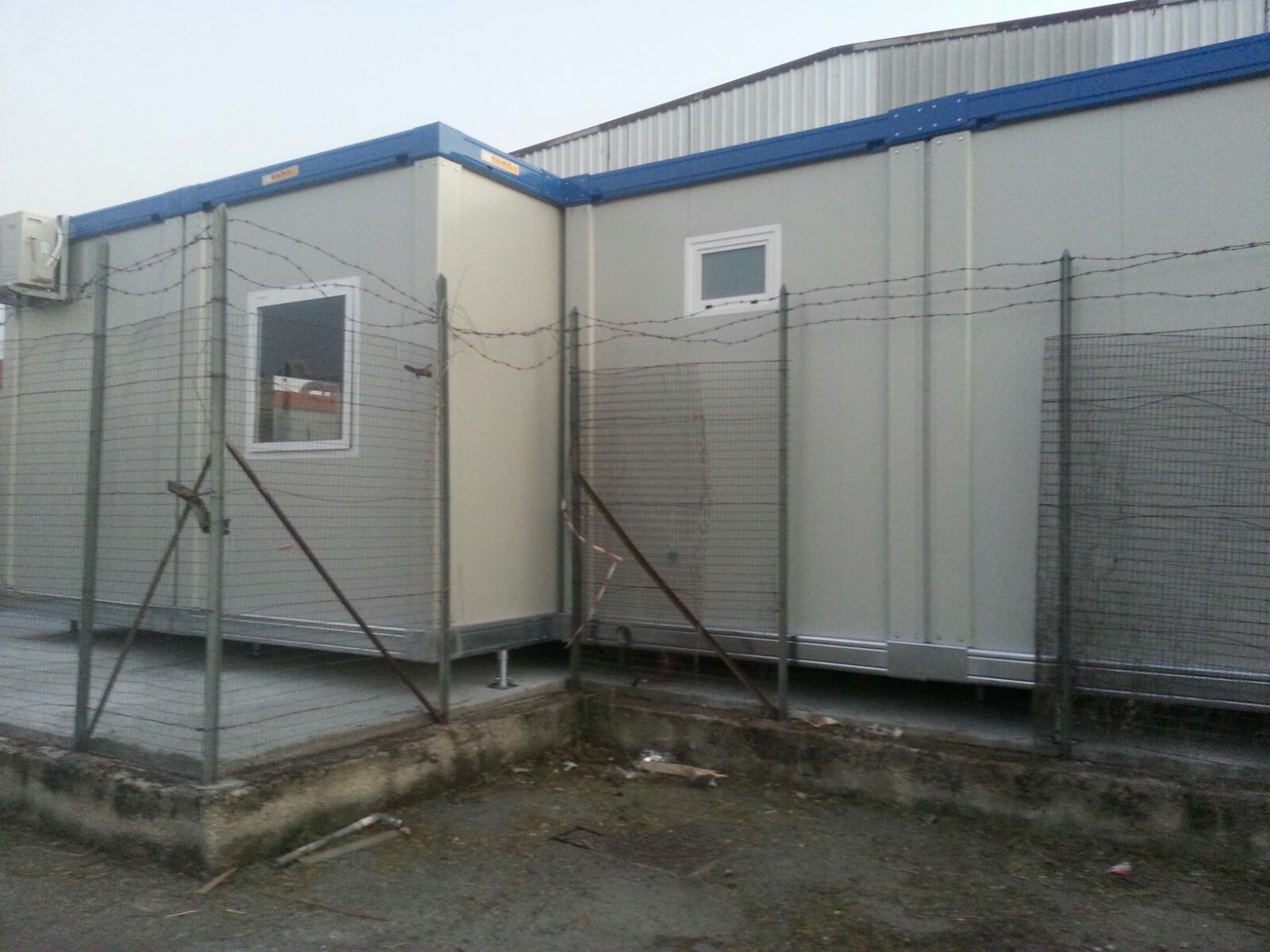 Dietro un recinto di filo spinato si trova un edificio bianco con il tetto blu