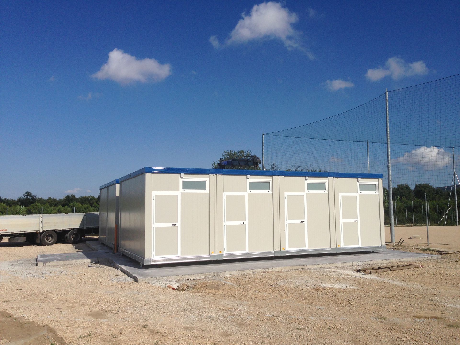 Un grande edificio bianco con il tetto blu si trova nel mezzo di un campo sterrato.