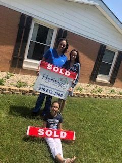 Two women and a child are holding a sold sign in front of a house.